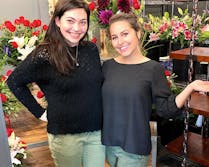 A pair of happy employees pose before dozens of beautiful bouquets